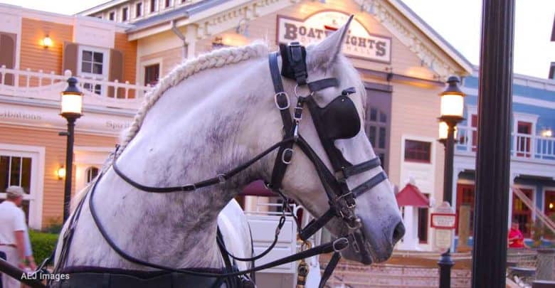 A white horse with a braided mane and festive harness awaits guests outside a vibrant building in the park’s main plaza.