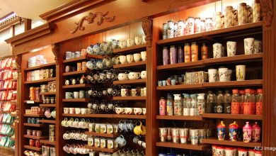 Brightly lit shelves stocked with Disney-themed mugs, colorful souvenir cups, bottles, and snacks at a theme park gift shop.