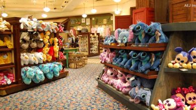 A store brimming with colorful stuffed animals and plush toys, reminiscent of Disney Resort perks. Shelves host a variety of characters, including large blue and pink ones, with more toys adorning the walls. Patterned carpeting and warm lighting enhance the enchanting atmosphere.