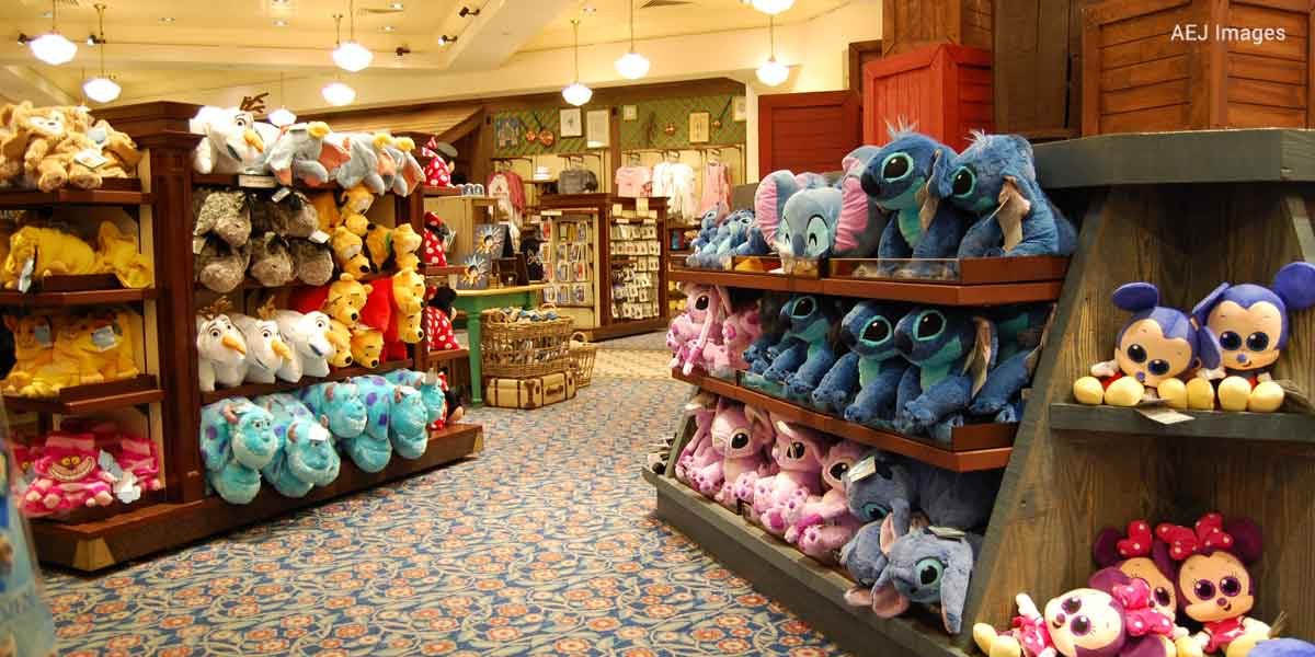 A store brimming with colorful stuffed animals and plush toys, reminiscent of Disney Resort perks. Shelves host a variety of characters, including large blue and pink ones, with more toys adorning the walls. Patterned carpeting and warm lighting enhance the enchanting atmosphere.