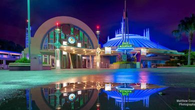 Space Mountain glows at night during Disney After Hours, colorful lights shimmering in puddles and a purple sky over an empty entrance.