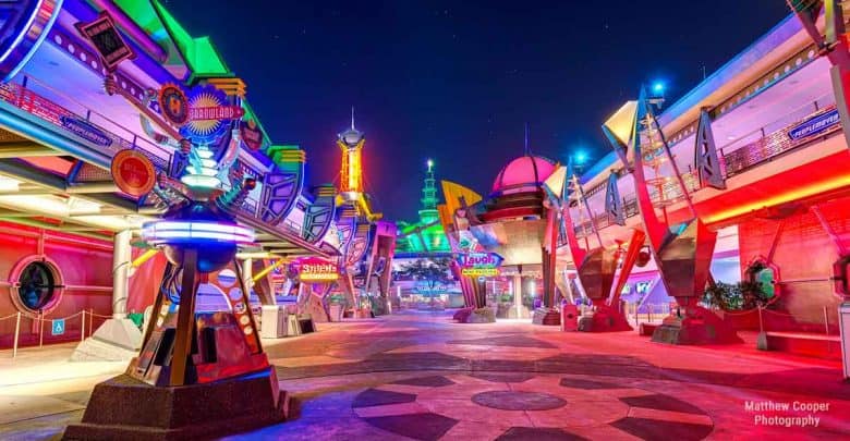 Vibrant neon-lit avenue glows after dark in Tomorrowland, featuring sleek sci-fi architecture and an inviting, crowd-free vibe.
