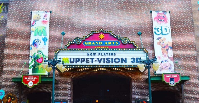 Entrance to Muppet*Vision 3D at Grand Arts Theatre with a marquee sign, character banners, and Disney FastPass+ and wait time signs visible against a brick wall.