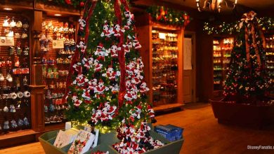 A festive store interior featuring decorated Christmas trees adorned with plush Mickey Mouse ornaments celebrates the magic of Holidays at Disney, surrounded by shelves of holiday decorations and souvenirs. Warm lighting creates a cozy, cheerful atmosphere.