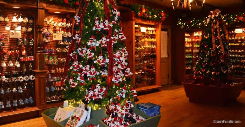 A festive store interior featuring decorated Christmas trees adorned with plush Mickey Mouse ornaments celebrates the magic of Holidays at Disney, surrounded by shelves of holiday decorations and souvenirs. Warm lighting creates a cozy, cheerful atmosphere.