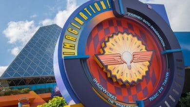 The sign for "Journey into Imagination" at the theme park pops with colorful designs and geometric shapes. A futuristic building with a glass pyramid structure gleams in the background against a blue sky—a hidden gem often overlooked in lists of rides to skip at Walt Disney World.