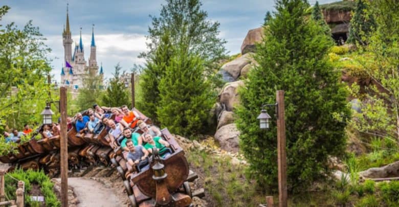 A roller coaster with passengers whirls through a curve, surrounded by lush greenery. In the distance, a castle with tall spires stands majestically against the cloudy sky. This enchanting scene, reminiscent of Magic Kingdom rides, is brimming with excitement and wonder.