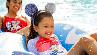 A child wearing glittery mouse ears and a colorful swimsuit smiles while at a water park