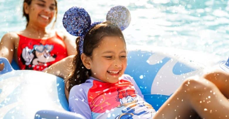 A child wearing glittery mouse ears and a colorful swimsuit smiles while at a water park