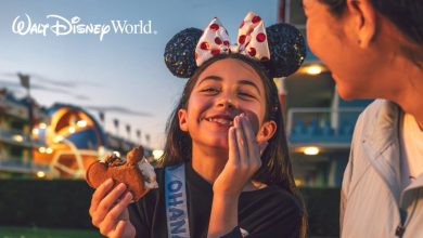 A young girl wearing Mickey Mouse ears and a sash smiles while holding a Mickey-shaped ice cream sandwich, sitting next to an adult at Walt Disney World. They’re clearly enjoying the magic—a reminder to focus on fun and know what to avoid at Disney World.