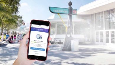 A person holds a smartphone displaying a food order screen in front of Cosmic Ray’s Starlight Café at Magic Kingdom.