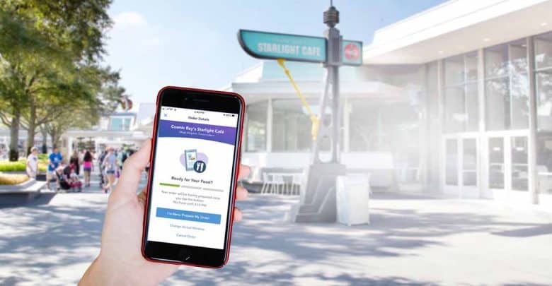 A person holds a smartphone displaying a food order screen in front of Cosmic Ray’s Starlight Café at Magic Kingdom.