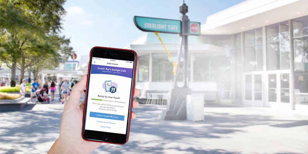 A person holds a smartphone displaying a food order screen in front of Cosmic Ray’s Starlight Café at Magic Kingdom.