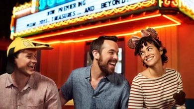 Three people sit in front of a brightly lit theater marquee at Walt Disney World.