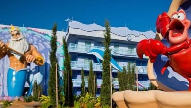 King Triton and Sebastian statues welcome guests outside Disney’s Art of Animation Resort, set against a brilliant blue sky.