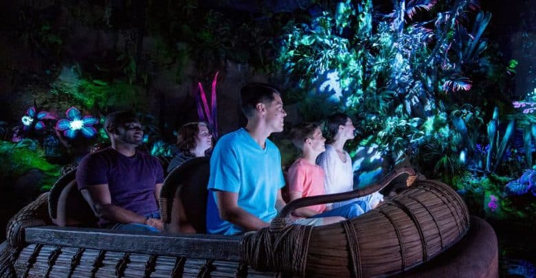 A group of five people enjoys a dark, immersive ride that could be on any Ultimate Disney Ride List for Little Ones, with glowing plants and flowers surrounding them. The dimly lit setting features vibrant blues, pinks, and purples, creating a magical atmosphere.