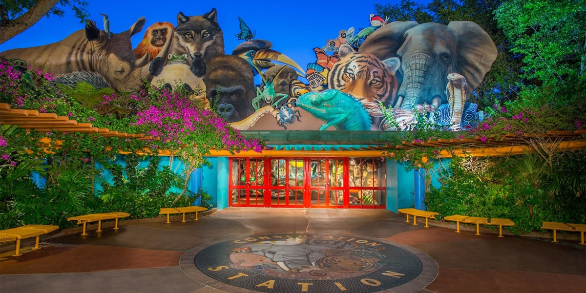 Entrance to Conservation Station at Disney’s Animal Kingdom, highlighted in the Disney’s Animal Kingdom Guide, features a vibrant mural of large animal faces above red doors, framed by lush plants and benches.