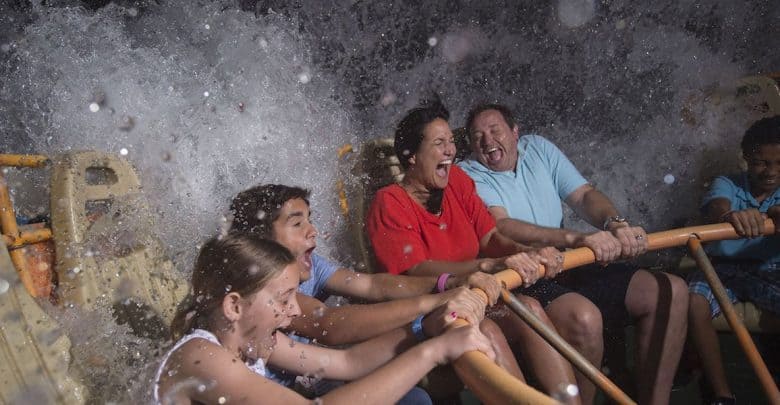 Four people laugh and scream as a large wave splashes over them on a water ride, gripping the safety bars for support. Water droplets fill the air—one of the best Disney World heat tips for cooling off and capturing the thrill of the moment.