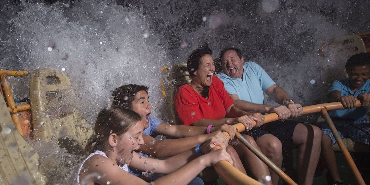 Four people laugh and scream as a large wave splashes over them on a water ride, gripping the safety bars for support. Water droplets fill the air—one of the best Disney World heat tips for cooling off and capturing the thrill of the moment.
