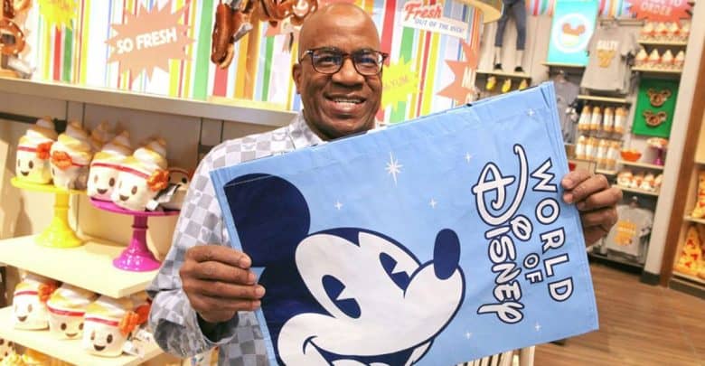 A man smiles while holding a blue "World of Disney" bag featuring Mickey Mouse, enjoying the colorful displays and Disney merchandise—proof that staying cool at Disney is all about finding magic indoors.