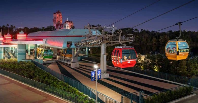 A Disney Skyliner gondola station at night, with colorful cabins gliding along cables. The area is well-lit, and the Twilight Zone Tower of Terror looms in the background—perfect for guests seeking Disney park exit tips after a magical day.
