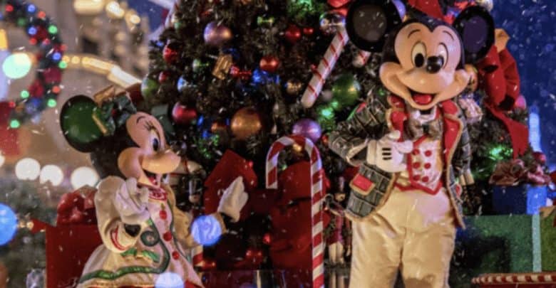 Mickey and Minnie Mouse are dressed in festive holiday outfits at Disney World, standing in front of a large decorated Christmas tree with presents underneath. Snow is gently falling, creating a cheerful, wintry scene.