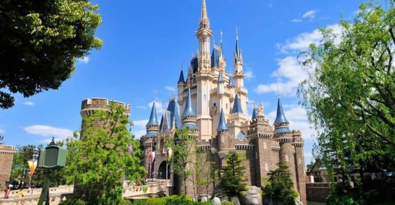 Cinderella Castle with its iconic blue spires rises above lush trees beneath a vivid blue sky in Magic Kingdom Park.