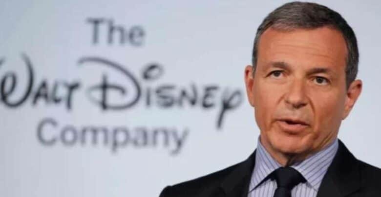 A man in a suit speaks in front of a screen displaying "The Walt Disney Company" logo.