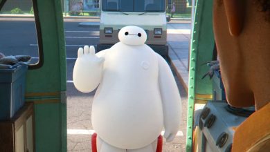 Baymax enthusiastically waves hello outside a food truck, as seen from the interior during Disney park festivities.