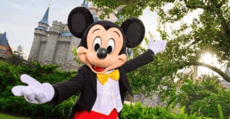Mickey Mouse welcomes guests with open arms in front of Cinderella Castle at Disney World, surrounded by lush greenery.