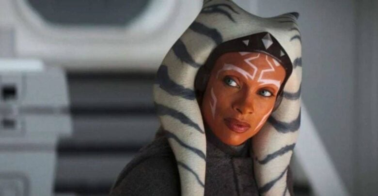 A person with orange skin, white facial markings, and a headpiece with long, striped lekku looks attentively to the side. They are wearing a dark robe, set against a gray, futuristic background.