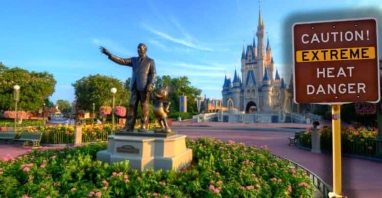 A statue of a man and a mouse stands in a garden near a castle, with clear blue skies overhead. A sign nearby reads "CAUTION! EXTREME HEAT DANGER," indicating potential weather hazards in the area. The scene has that magical Disney theme park charm.