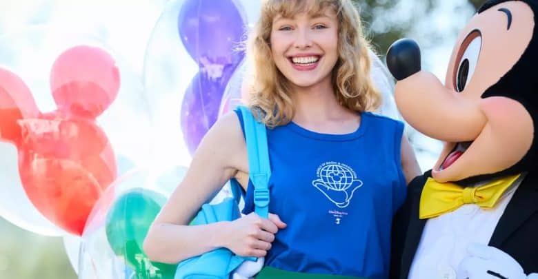 Smiling person wearing a blue backpack and top stands next to a Mickey Mouse costumed character, with colorful Mickey-shaped balloons in the background—capturing true Walt Disney World Essentials.