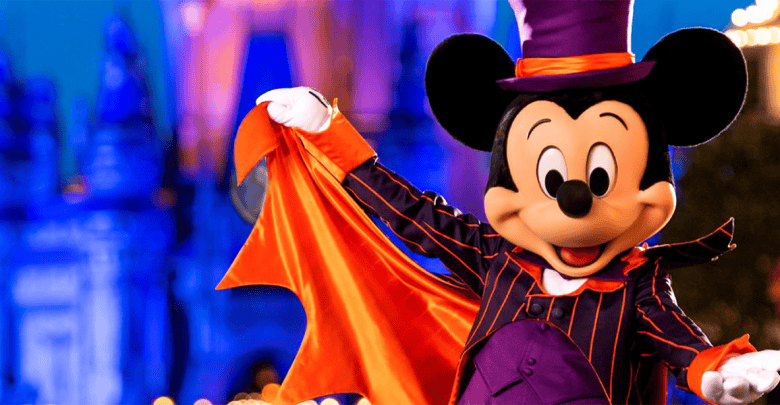 Mickey Mouse dressed in a black and orange striped suit, with a matching top hat and cape, posing in front of a brightly lit castle at night. The background includes vibrant blue and purple lighting, creating a festive and magical atmosphere.