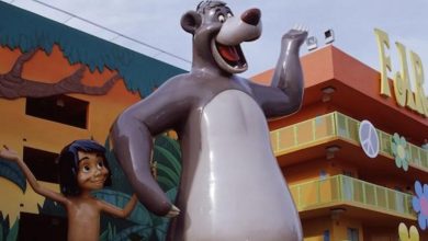 A statue of Baloo the bear and Mowgli from The Jungle Book stands in front of a colorful building at the Best Disney Value Resort, decorated with vibrant murals, peace signs, and flowers.