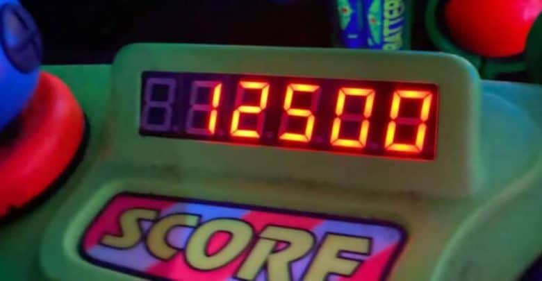 A digital display shows a score of 125,000 in bright red numbers. The word "SCORE" is prominently displayed below the score on a colorful, decorative panel. Parts of blue and red buttons are visible in the background.