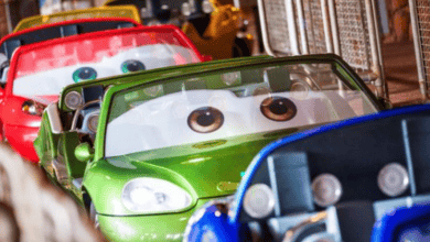 Colorful cartoon-themed cars line up on a track at Disneyland, each with large expressive eyes on the windshields. These vibrant vehicles resemble animated characters, featuring lively hues like green, red, and blue.