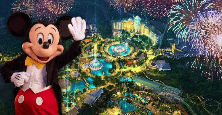 Mickey Mouse waves in front of a vibrant aerial view of Disney World at night, where colorful fireworks illuminate the sky. In the distance, various attractions and structures shimmer below, a reminiscent spark against whispers of abandonment by 2025.