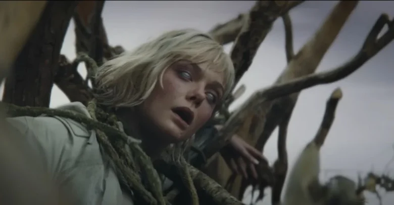 A woman with pale skin and blonde hair appears lifeless, her eyes rolled back. She is entangled in ropes and surrounded by dried, broken cornstalks under an overcast sky.