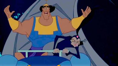 A muscular man in blue and yellow armor joyfully raises his arms while sitting in a cart next to a thin woman in black with a tall headpiece, who looks annoyed. Both characters appear animated and are in motion.