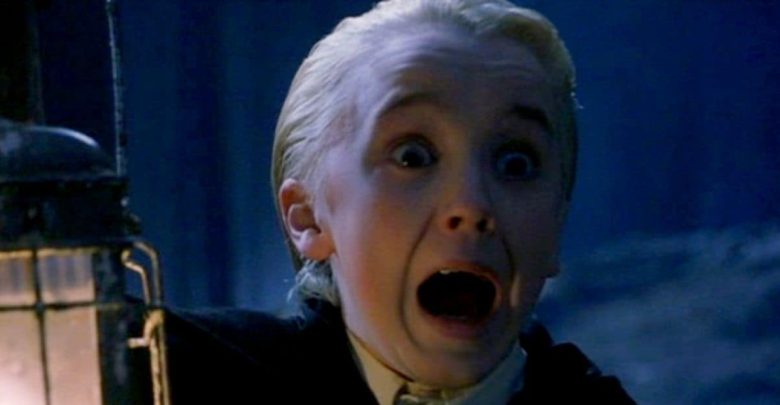 A young boy with slicked-back blond hair screams in fear while holding a lantern in a dark, eerie setting. His eyes are wide, and his mouth is open in shock.