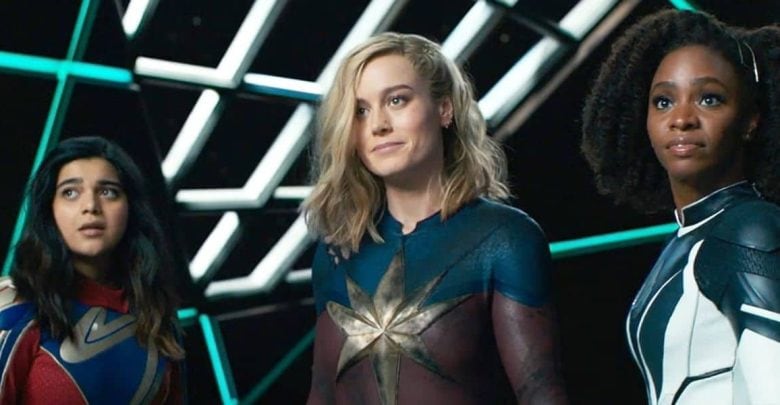 Three women in superhero costumes stand together in a futuristic, geometric-lit setting, looking forward with serious and determined expressions.