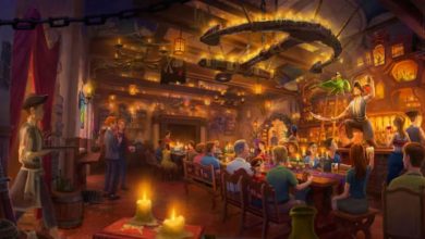 A lively, warmly lit tavern scene with people eating, drinking, and socializing. Amidst Disney World Renovations, a performer with a green bird captivates patrons as candles, wooden furniture, and rustic decor fill the bustling room.