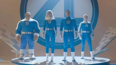Four people wearing blue and white superhero costumes with the number "4" on their chests stand on a circular platform in front of a large "4" symbol, capturing the excitement as Kevin Feige talks about Fantastic 4. The scene features a bright, futuristic design.