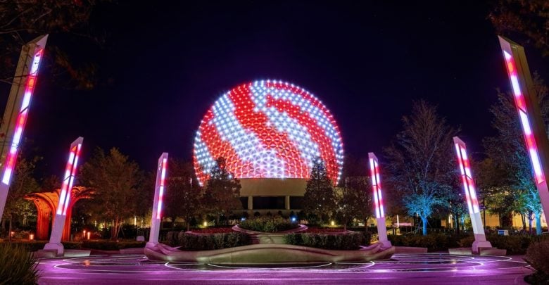 A large geodesic sphere is illuminated with swirling red and white lights at night, surrounded by glowing columns and trees, with circular patterns of light on the ground.