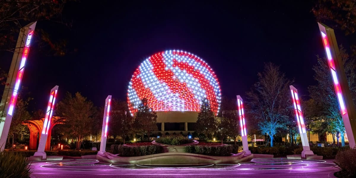 A large geodesic sphere is illuminated with swirling red and white lights at night, surrounded by glowing columns and trees, with circular patterns of light on the ground.