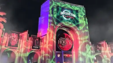 The entrance to Universal Studios Florida is lit up at night with colorful green and purple lights for Halloween Horror Nights, featuring spooky banners and event signage.