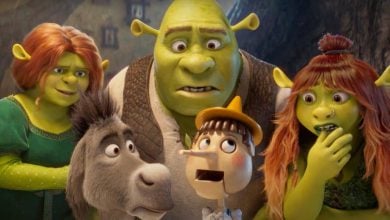 Five animated characters, including green ogres, a donkey, and a wooden puppet, look surprised and curious while standing close together, with a blurry forest background.