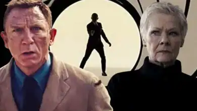 A serious man in a tan suit and a woman with short gray hair stand in front of the iconic James Bond gun barrel backdrop, with a silhouette of a man holding a gun visible in the center background.
