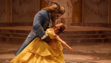 A woman in a yellow ball gown dances with a beastly figure in a blue suit in an ornate, golden ballroom, evoking a classic fairy tale scene.